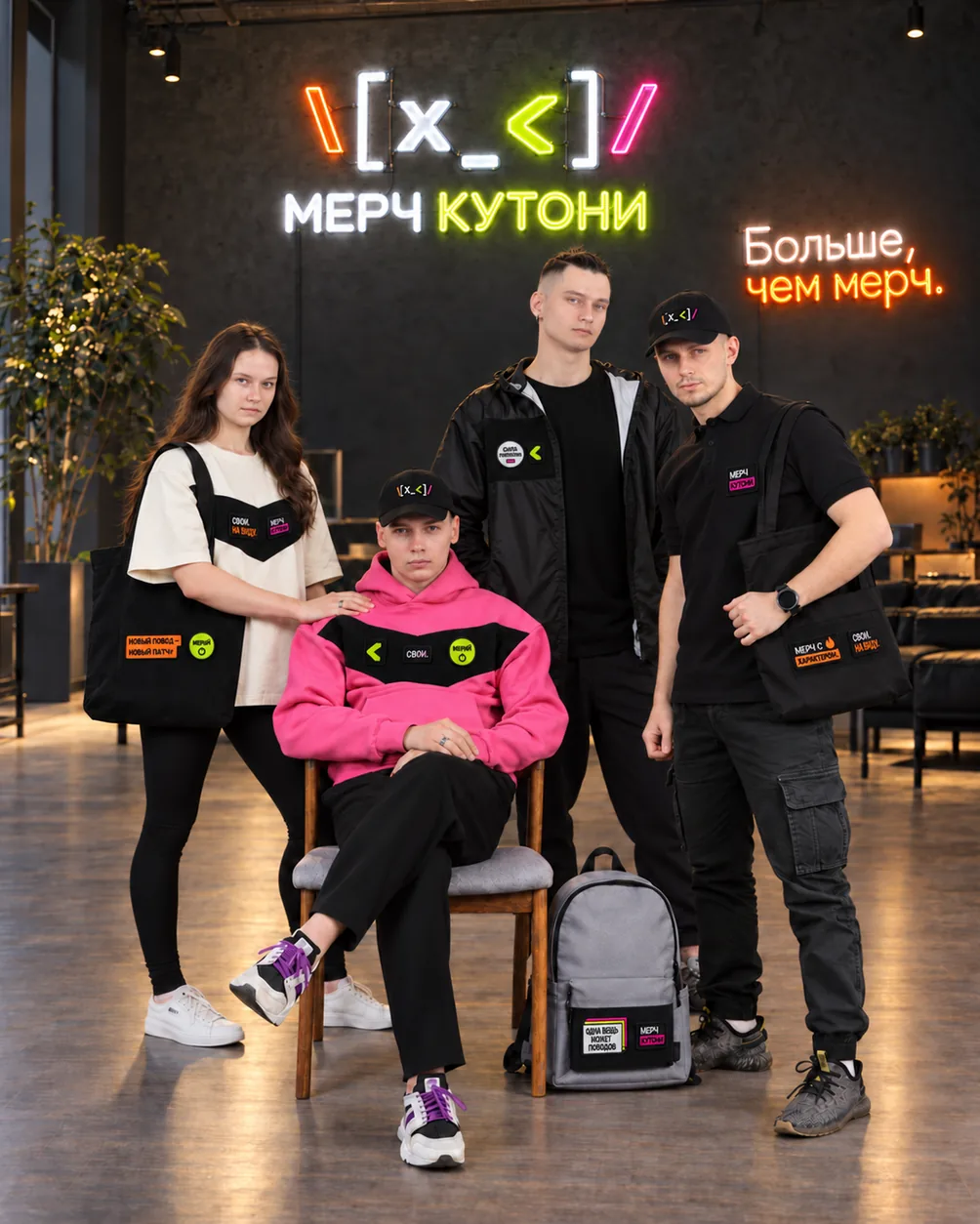 Four employees in merch with swappable patches in a studio with a neon sign