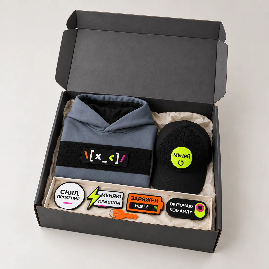 An open welcome pack box: hoodie, cap and swappable patches for a new hire